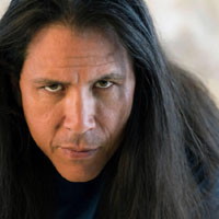 Long, dark hair frames the face of Sensei William Ford as he stares with an intense gaze.