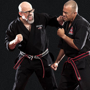 John Hackleman, dressed in a black martial arts uniform, makes eye contact with the camera.