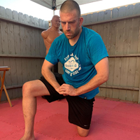 Joshua Loya kneels post-workout with hands in the GKKD bow.