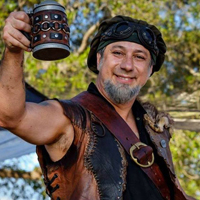 A smiling Daniel O'Ryan in Renaissance attire toasts a wooden beer mug.