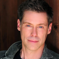 A headshot of Roy Samuelson with gleaming blue eyes leaning against a fence.