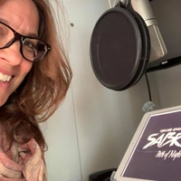 Nicol Zanzarella smiles off-camera to her side while sitting in front of a studio microphone and tablet.