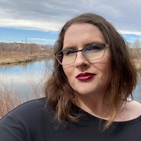 Erin Daley wears a slight smile as she poses in front of a lake and overcast sky.